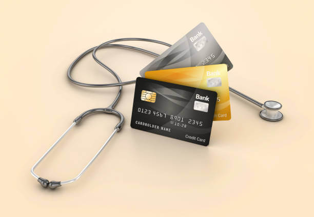 A stethoscope wrapped around a stack of three credit cards, suggesting a connection between healthcare costs and financial transactions