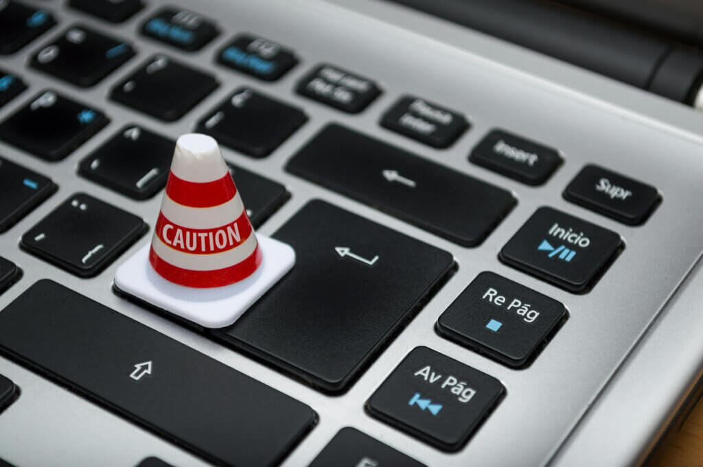 describe a small, red and white traffic cone with "CAUTION" written on it, placed on the keyboard of a laptop, specifically on the 'Enter' key. 