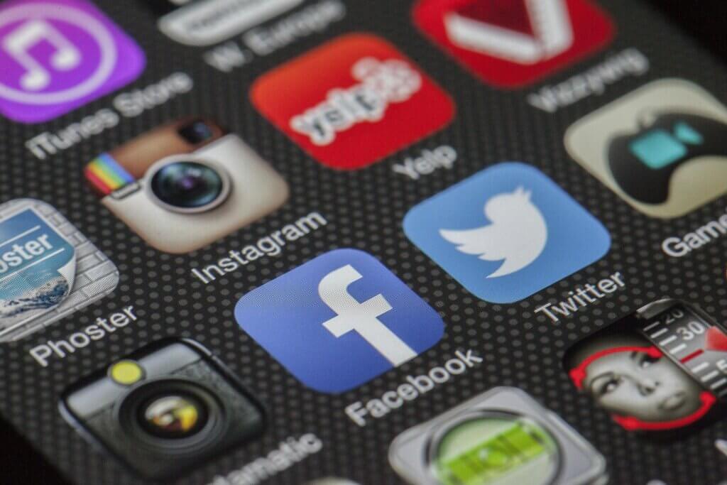 Close-up of a smartphone screen displaying various social media application icons, including Facebook, Twitter, Instagram, and YouTube